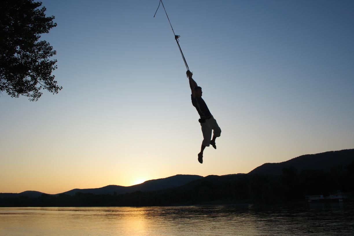 Figure on a rope swing over a body of water at sunset.