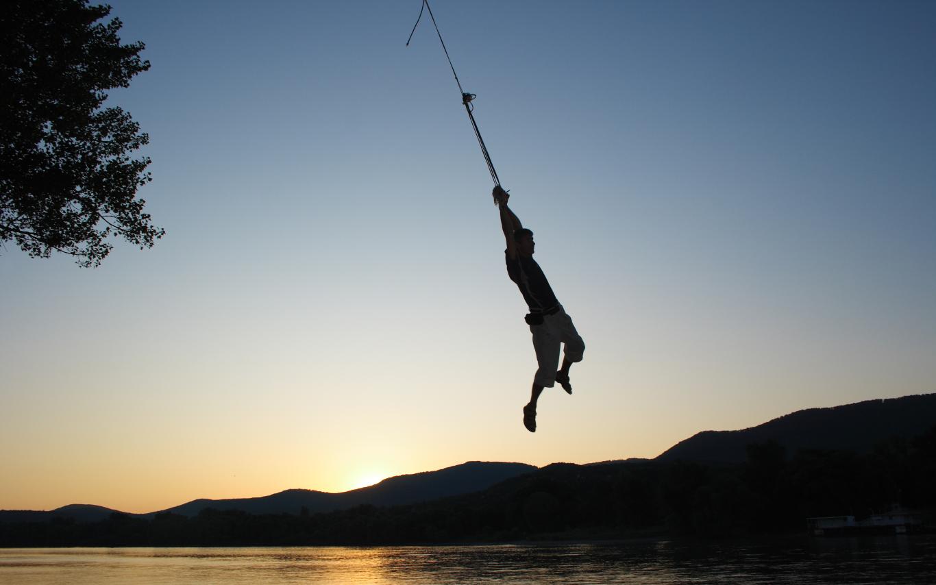 Figure on a rope swing over a body of water at sunset.